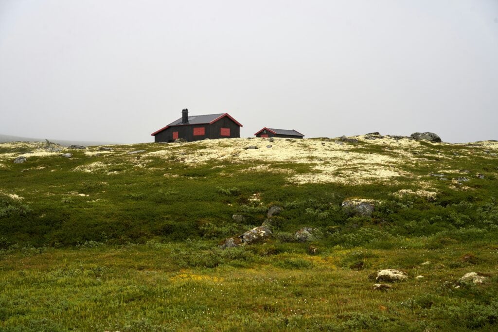 En isolert hytte på fjellet omgitt av grønt landskap og steiner, perfekt for en rolig ferie i naturen.