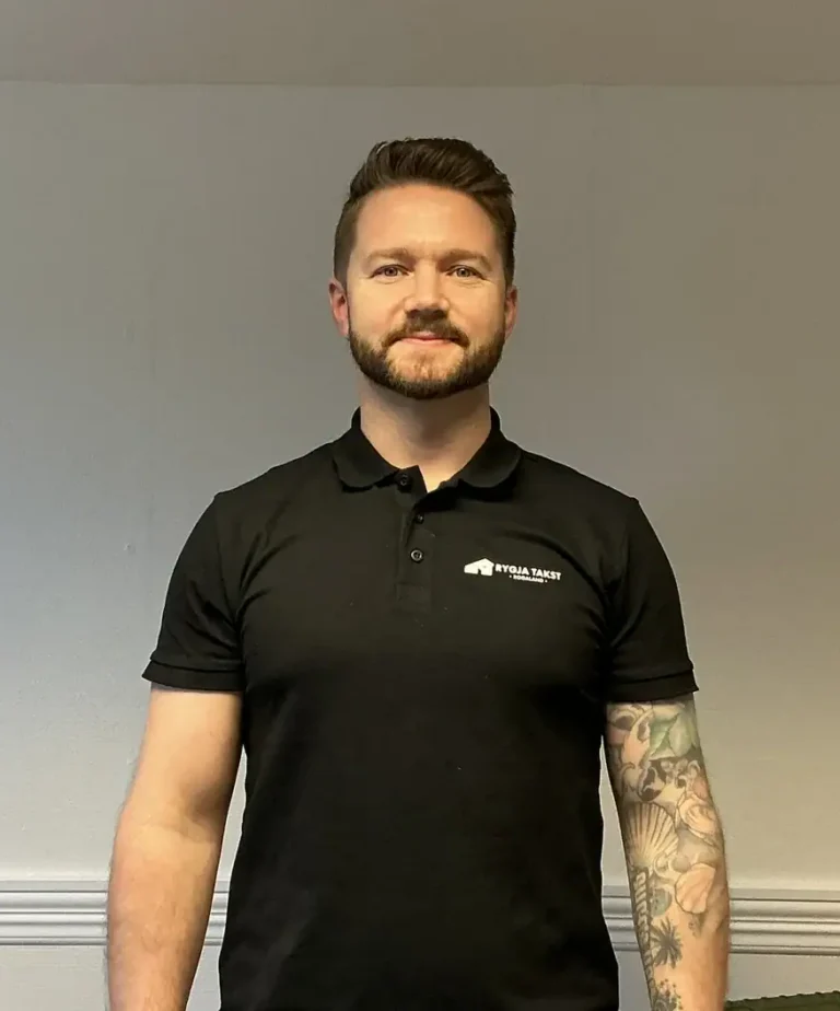 En mann i svart Rygja Takst-polo står innendørs med en vennlig holdning, klar til å utføre takseringstjenester for boligevaluering.